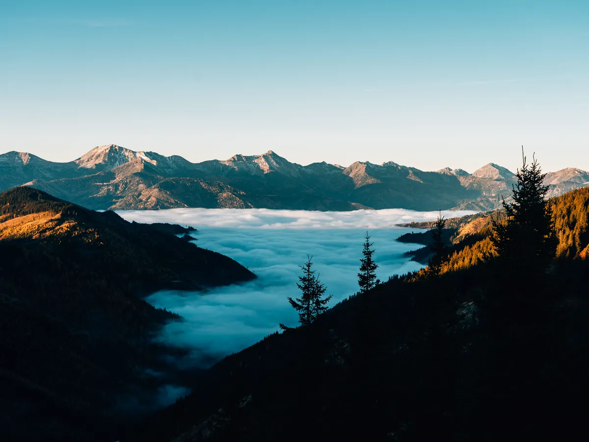 Fog sitting in a mountain valley below a ridge lit by early light