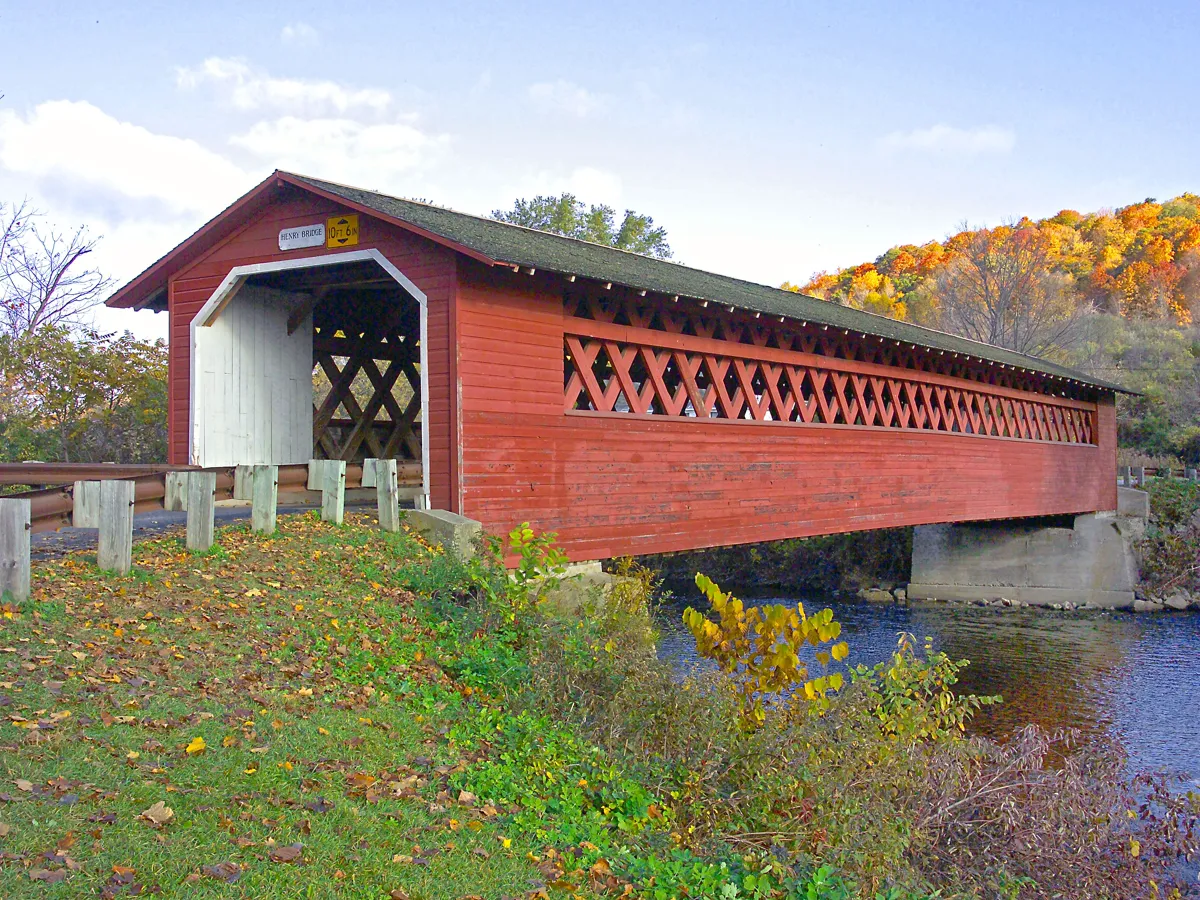 Wooden covered bridge over a shallow stream with sugar maples turning orange behind it